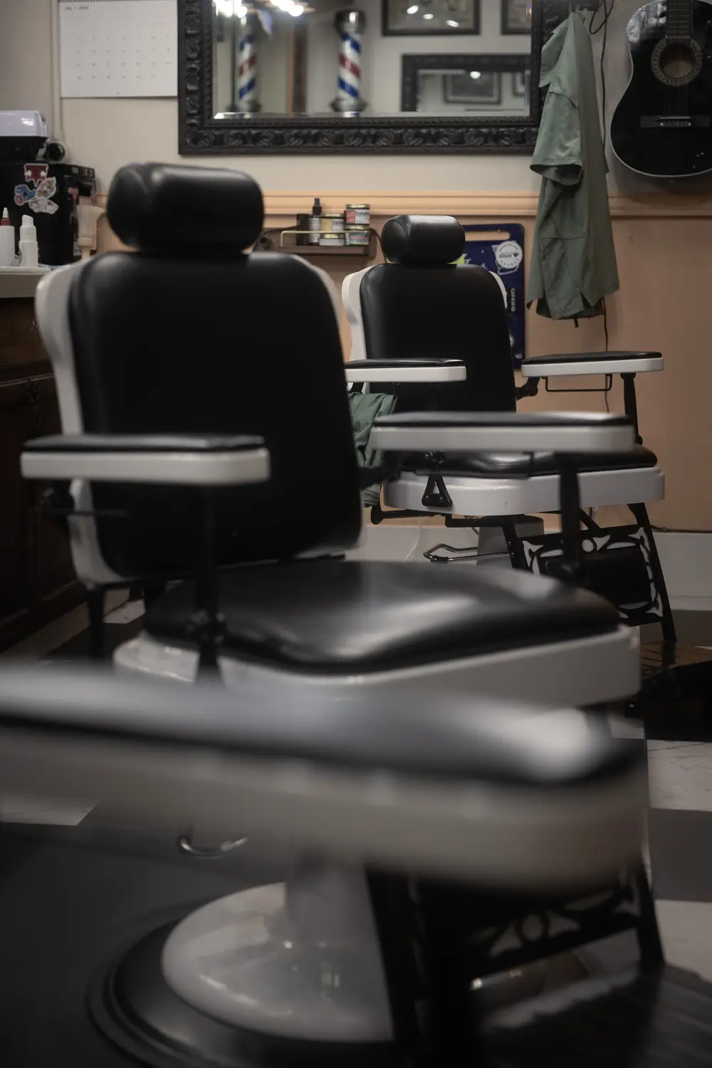 Two antique barber chairs facing the carved mirror, a barber pole reflected in it