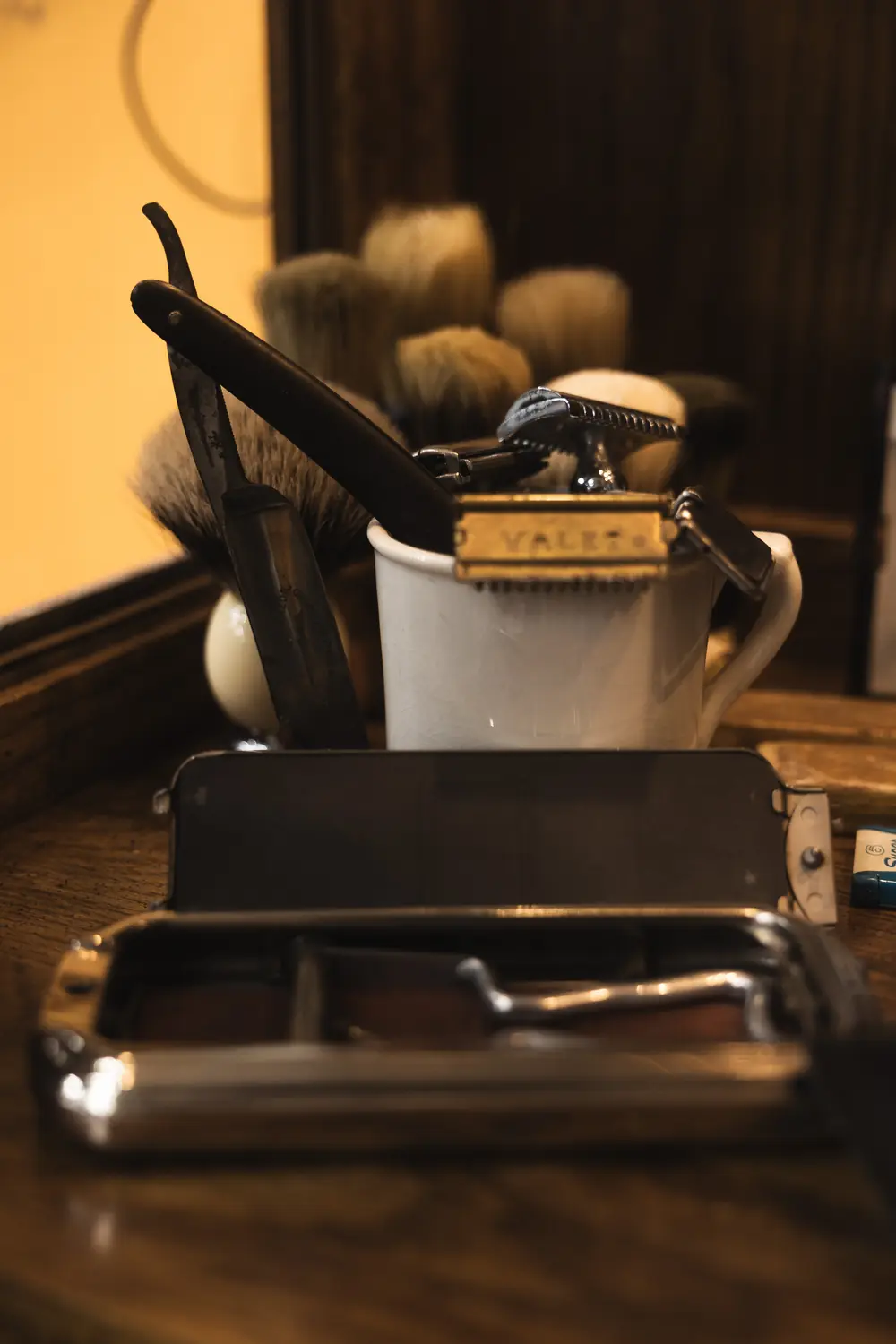 A straight razor, badger brushes and a shaving mug on the counter