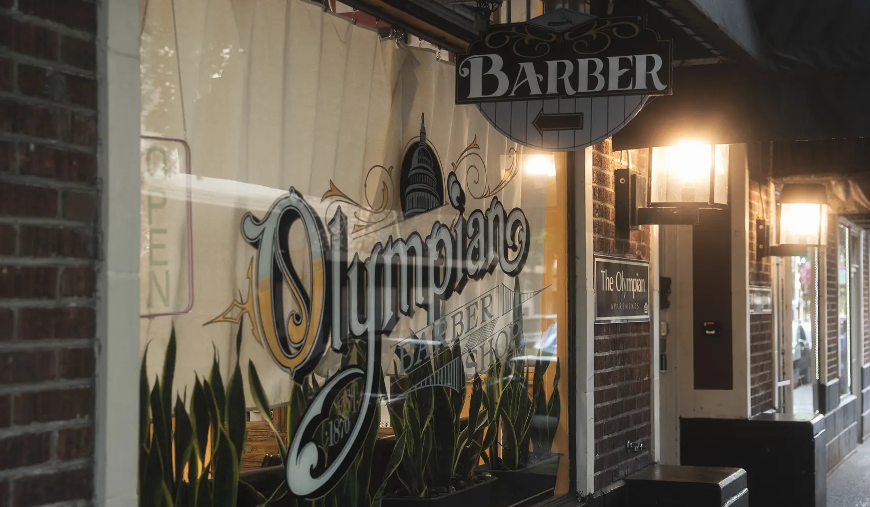 The Olympian Barbershop storefront on Washington Street, its name painted on the window beneath a hanging BARBER blade sign